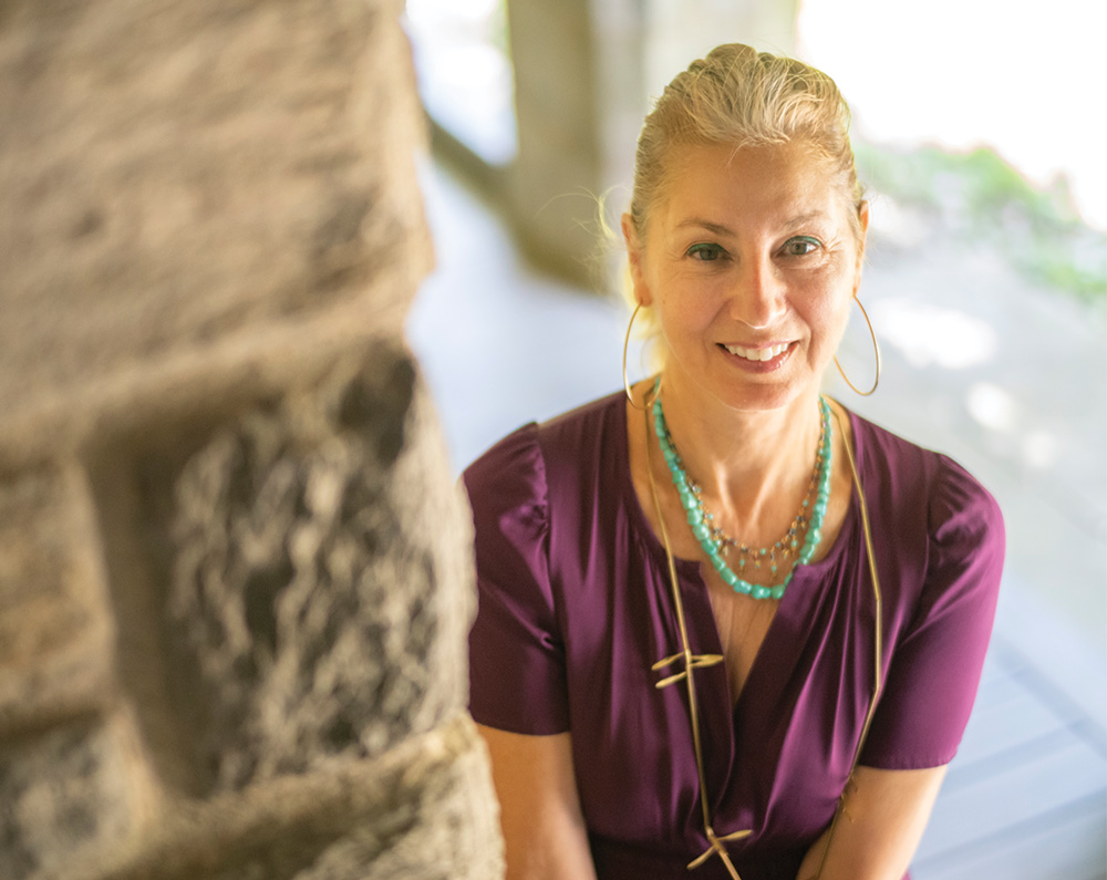 Jennifer Marks-Gold wears a purple dress, a turquoise necklace, and gold hoop earrings.