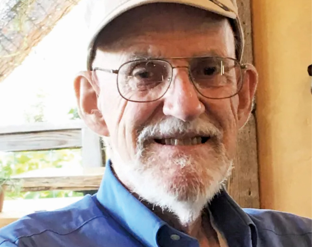 Raymond "Ray" Sawyer '53 wears a baseball cap,  glasses, and a blue collared shirt.