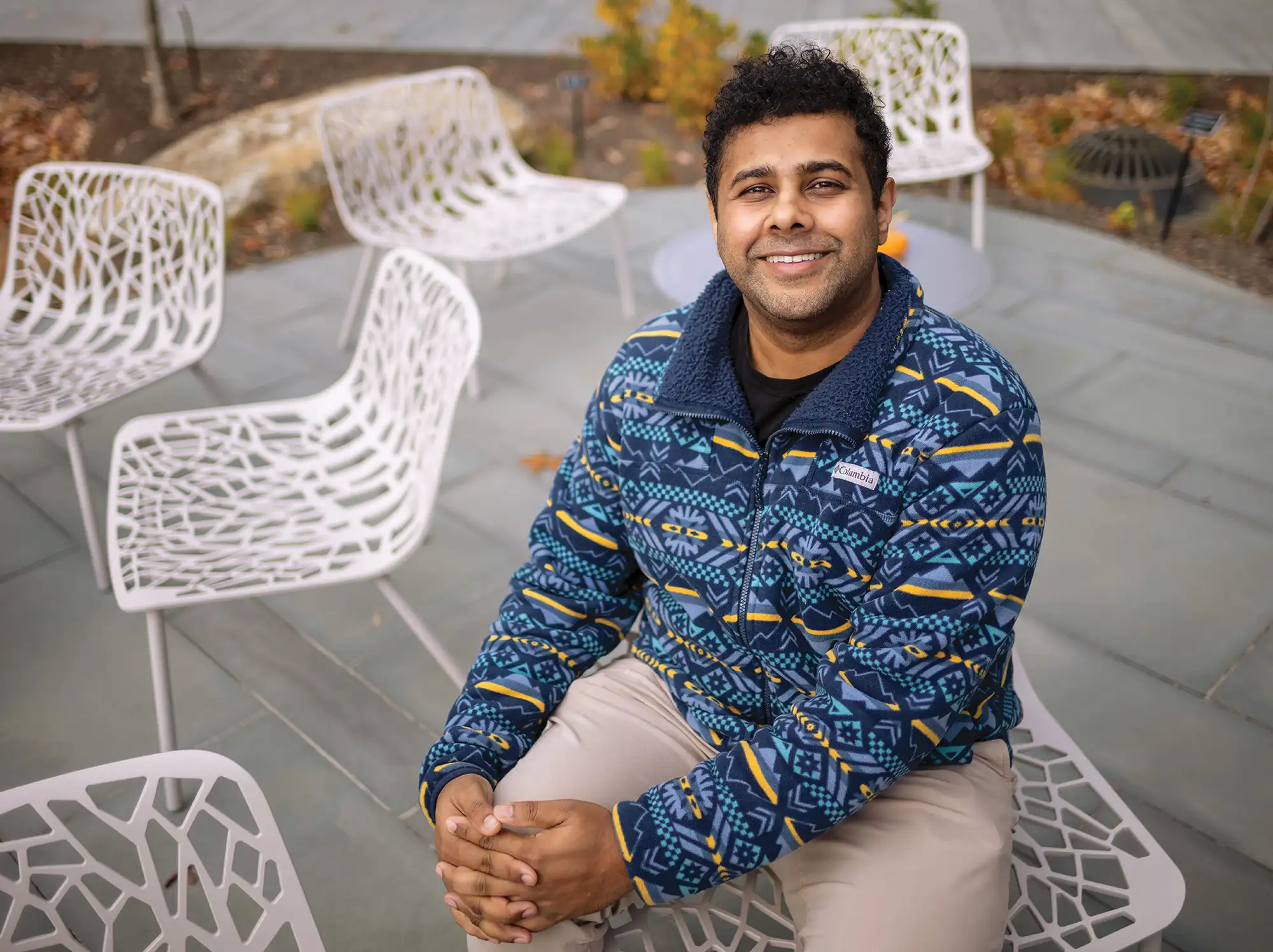 Sukrit Venkatagiri sits on a chair outside in a colorful pullover.