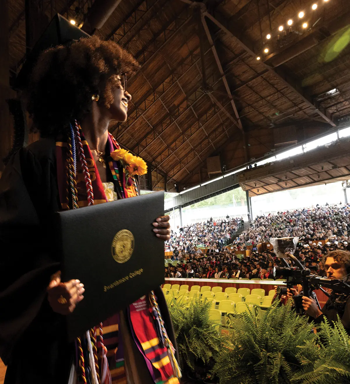 A student crosses the stage, holding their diploma and smiling at the crowd.