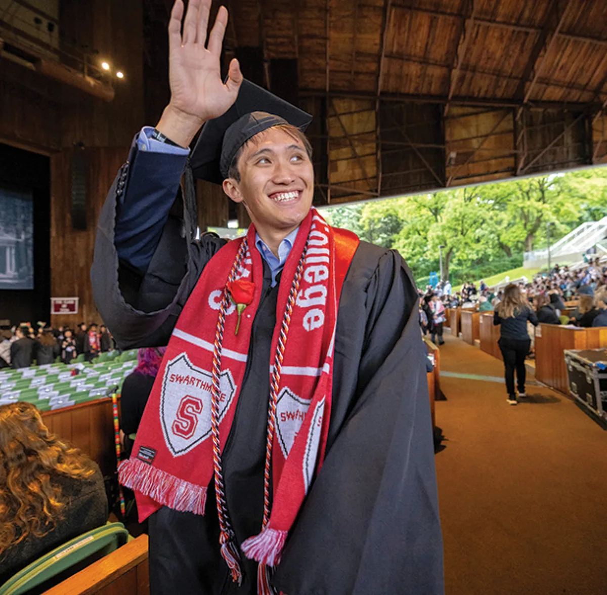 A student smiles and waves while crossing the graduation stage.